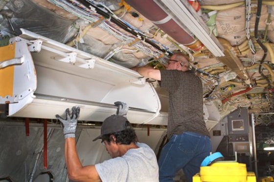 This undated photo provided by American Airlines parent company AMR shows workers installing larger bins for carry-on luggage on a Boeing 737 in Tulsa, Okla.